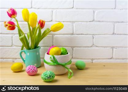 Easter rustic centerpiece with decorated eggs, green ribbon, red and yellow tulips in the polka dot mint green jug near painted brick wall