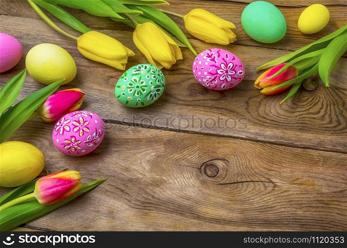 Easter rustic wooden background with pink and green floral decorated painted eggs and yellow red tulips. Happy Easter greeting card, copy space.