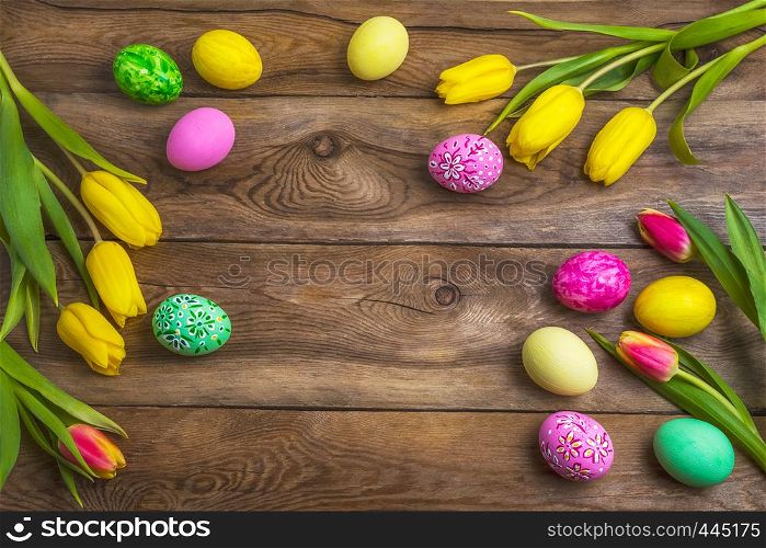 Easter rustic wooden background with pink, yellow and green painted eggs and tulips. Happy Easter greeting card, copy space.