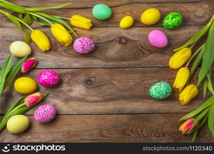 Easter rustic wooden background with yellow, pink and green floral decorated painted eggs and tulips. Happy Easter greeting card, copy space.