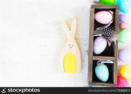 Easter scene with colored eggs and rabbit, flat lay on white wooden background. Easter colored eggs with tulips