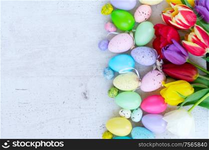 Easter scene with colored eggs and tulips border, flat lay on white wooden background. Easter colored eggs with tulips