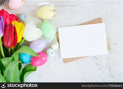 Easter scene with colored eggs and tulips, flat lay on white wooden background with copy space on card. Easter colored eggs with tulips