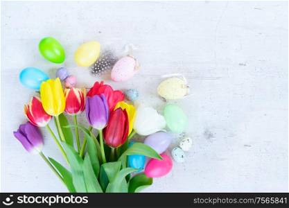 Easter scene with colored eggs and tulips, flat lay on white wooden background. Easter colored eggs with tulips