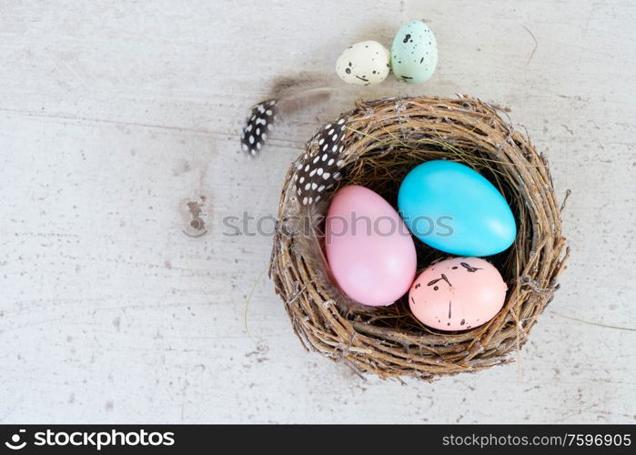 Easter scene with colored eggs in nest, flat lay on white wooden background with copy space. Easter colored eggs