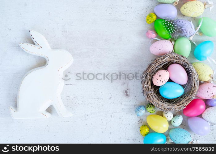 Easter scene with colored eggs, rabbit and tulips, flat lay on white wooden background with copy space. Easter colored eggs with tulips