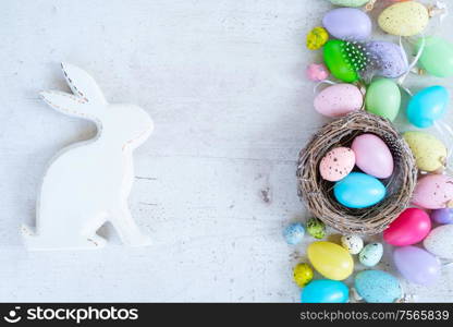 Easter scene with colored eggs, rabbit and tulips, flat lay on white wooden background with copy space. Easter colored eggs with tulips