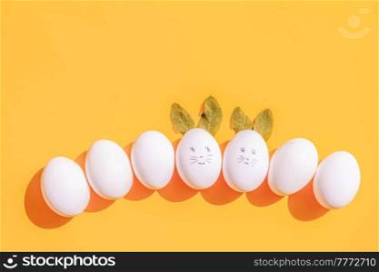 Easter scene with white eggs row with funny faces over illuminating yellow background. Easter scene with white eggs