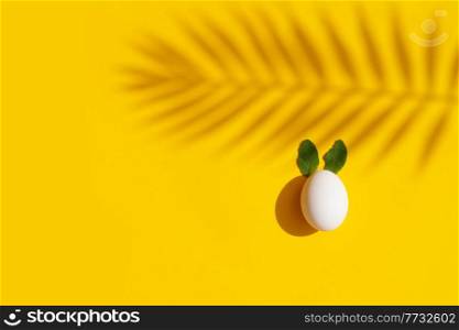 Easter scene with white eggs with rabbits ears over illuminating yellow background, palm shadows overlay. Easter scene with white eggs