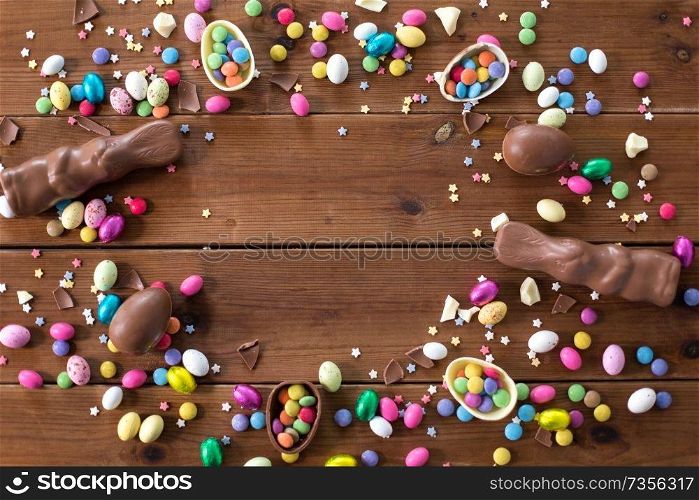 easter, sweets and confectionery concept - chocolate eggs, bunnies and candy drops on wooden background. chocolate eggs, easter bunnies and candies on wood