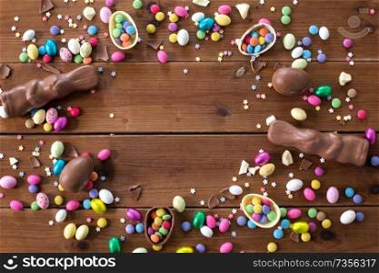 easter, sweets and confectionery concept - chocolate eggs, bunnies and candy drops on wooden background. chocolate eggs, easter bunnies and candies on wood