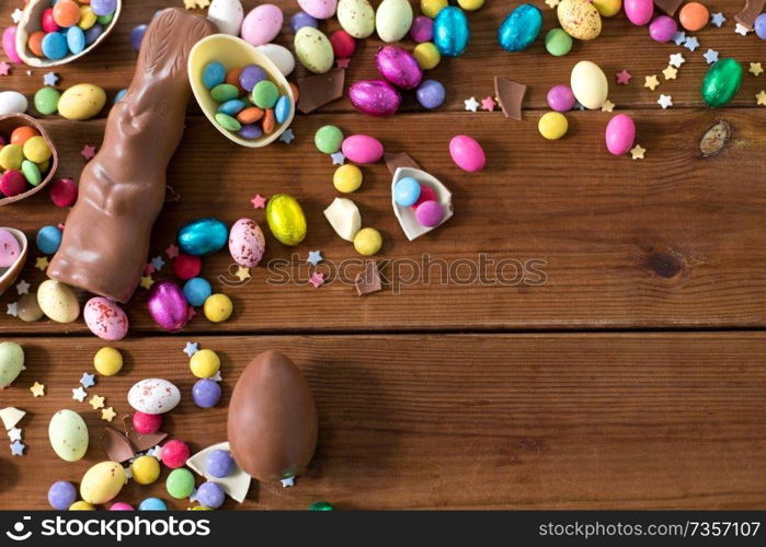 easter, sweets and confectionery concept - chocolate eggs, bunny and candy drops on wooden background. chocolate eggs, easter bunny and candies on wood