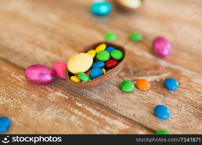 easter, sweets and confectionery concept - close up of chocolate egg and candy drops on wooden table. chocolate egg and candy drops on wooden table