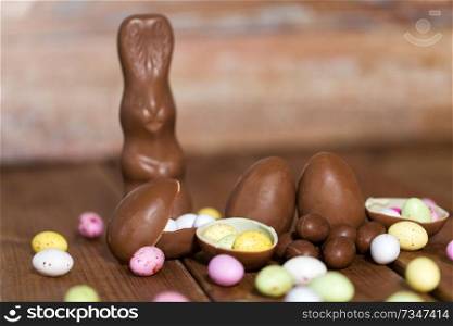 easter, sweets and confectionery concept - close up of chocolate eggs, bunny and candy drops on wooden table. chocolate eggs, easter bunny and candies on wood