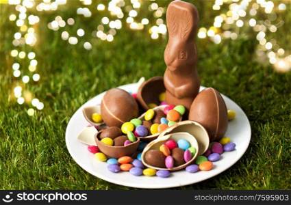 easter, sweets and confectionery concept - plate with chocolate bunny, eggs and candy drops on grass. chocolate bunny, eggs and candy drops on plate