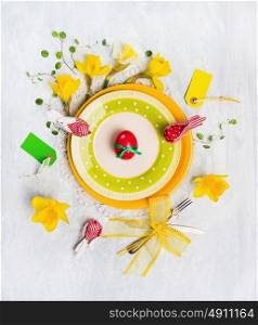 Easter table decoration with red egg, spring flowers, sign, knife and fork on yellow plate, top view