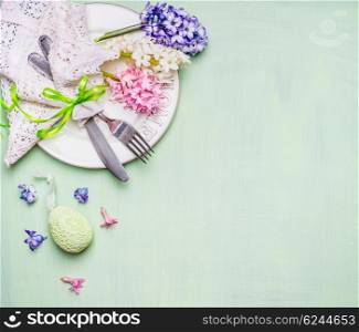 Easter table place setting with flowers and egg on light green background, top view. Place for text or Easter meal.