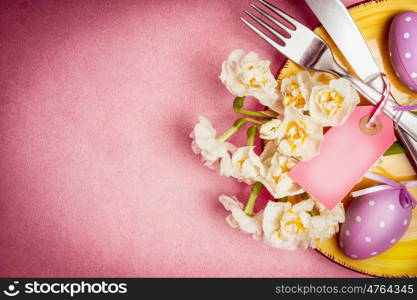 Easter table setting with plate, cutlery, flowers ,eggs and blank tag on pink background, top view, place for text