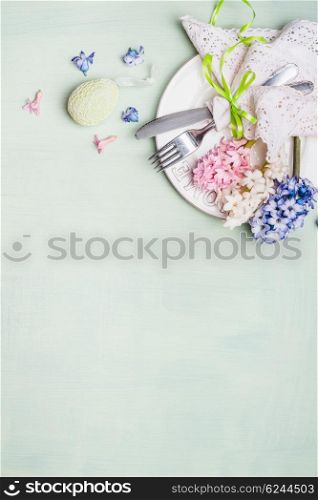 Easter table setting with plate, cutlery, lace doily napkin, hyacinths flowers and decor egg on light shabby chic wooden background, top view, vertical