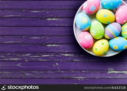 easter, tradition and object concept - close up of colored eggs on plate over ultra violet wooden boards background. close up of colored easter eggs on plate