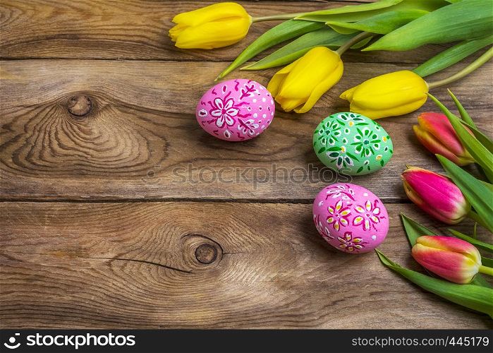 Easter wooden background with pink and green floral decorated painted eggs and yellow red tulips. Happy Easter greeting card, copy space.