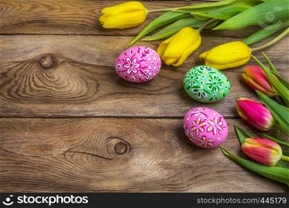 Easter wooden background with pink and green floral decorated painted eggs and yellow red tulips. Happy Easter greeting card, copy space.