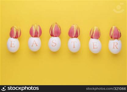 Easter word wrote on eggshells with tulips inside them on a yellow background. Flat lay with copy space