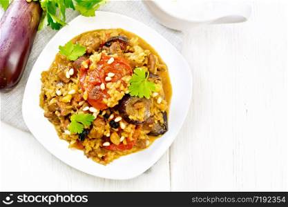 Eastern and European national dish of maklube made of rice, eggplant, tomatoes, spices and garlic in a plate on a napkin on the background of light wooden board from above
