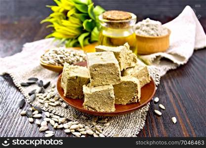 Eastern sweet halva sunflower in a plate, sunflower seeds, oil, flour and flower on a sacking on a background of a dark wooden board