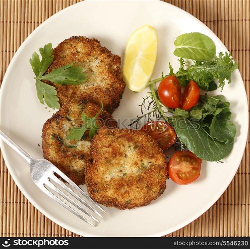 Easy to make fishcakes, with steamed fish crumbled into mashed potato and parsley mix, thickened with some flour, rolled in breadcrumbs and fried, served with a salad. High angle view