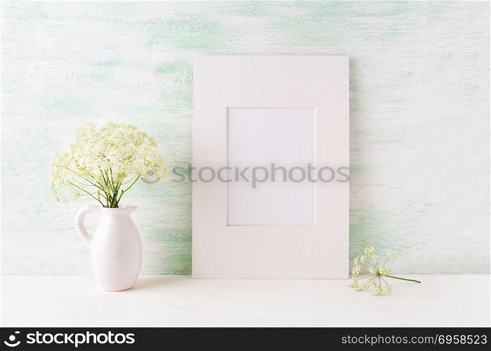 Easy white frame mockup with tender wild flowers in pitcher. Empty frame mock up for presentation artwork.. Easy white frame mockup with tender wild flowers in pitcher