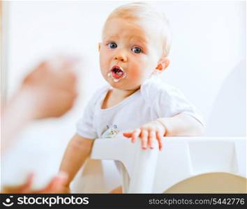 Eat smeared adorable baby girl in baby chair feeding by mother&#xA;