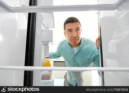 eating and diet concept - confused middle-aged man looking for food in empty fridge at kitchen. man looking for food in empty fridge at kitchen