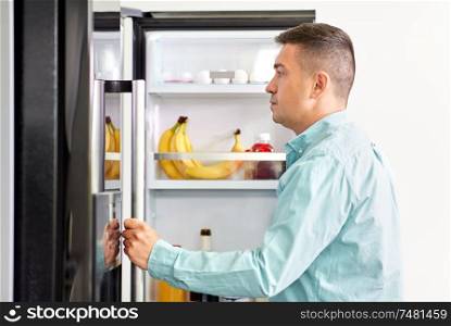 eating and diet concept - middle-aged man looking for food in fridge at kitchen. man looking for food in fridge at kitchen