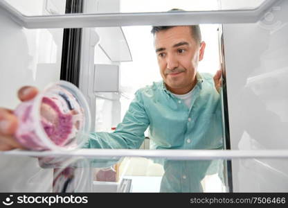 eating and diet concept - middle-aged man taking container with food leftovers from fridge at kitchen. man taking empty food container from fridge