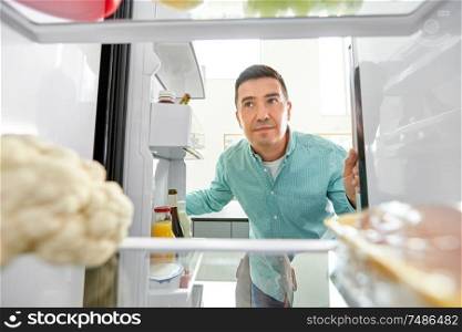eating and diet concept - smiling middle-aged man looking for food in fridge at kitchen. man looking for food in fridge at kitchen