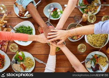 eating and leisure concept - group of people having dinner and holding hands together over table with food. people holding hands together over table with food