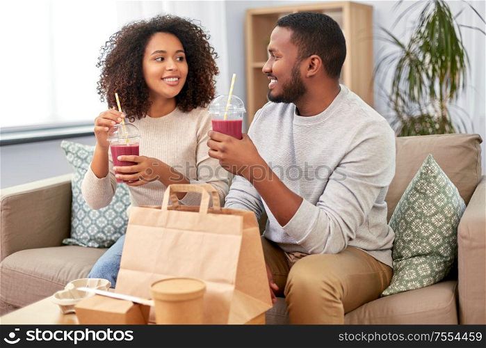 eating and people concept - happy african american couple with takeaway food and drinks at home. happy couple with takeaway food and drinks at home