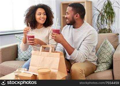 eating and people concept - happy african american couple with takeaway food and drinks at home. happy couple with takeaway food and drinks at home
