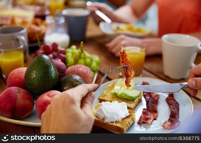 eating and people concept - male hands with knife and bacon on fork at table full of food. hands with bacon on fork at table full of food