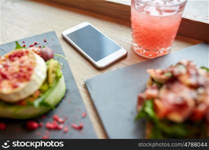 eating and technology concept - smartphone and glass of drink with food at restaurant or cafe