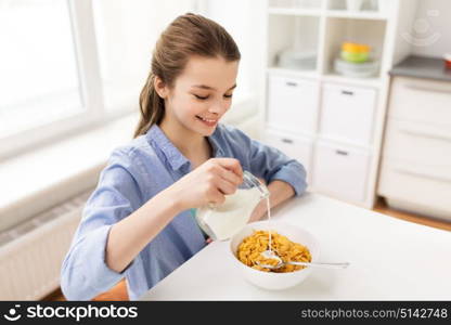 eating, breakfast and people concept - happy girl pouring milk to bowl with corn flakes at home kitchen. happy girl having breakfast at home kitchen