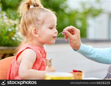 eating, childhood and people concept - mother hand with spoon feeding daughter at cafe. mother hand with spoon feeding daughter at cafe