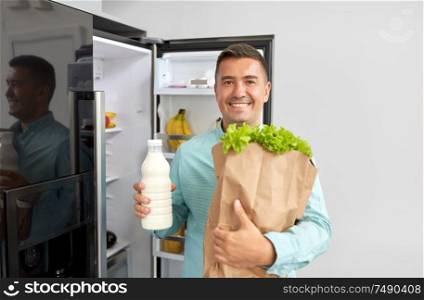 eating, diet and storage concept - smiling middle-aged man with new purchased food in paper bag at home fridge. man with new purchased food at home fridge