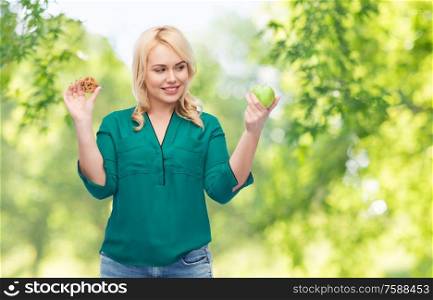eating, food and diet concept - happy smiling woman choosing between apple and cookie over green natural background. smiling woman choosing between apple and cookie