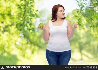 eating, food and diet concept - plus size woman choosing between apple and donut over green natural background. plus size woman choosing between apple and donut