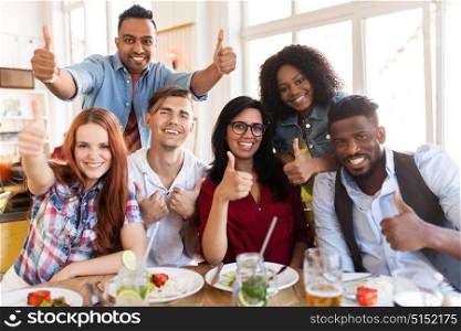 eating, food and people concept - group of happy international friends showing thumbs up gesture at restaurant table. happy friends showing thumbs up at restaurant