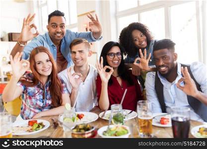 eating, food and people concept - group of happy international friends showing ok hand sign at restaurant table. happy friends showing ok hand sign at restaurant