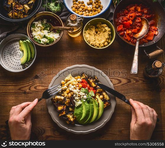 Eating healthy vegetarian meal in bowl with chick peas puree, roasted vegetables , red paprika tomatoes stew, avocado and seeds . Clean or dieting, vegetarian food concept