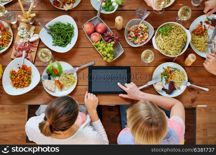 eating, people and technology concept - women with tablet pc computer sitting at table full of food. women with tablet pc at table full of food